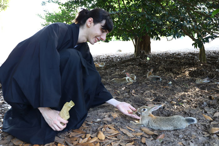 Okunoshima rabbit island | Japan City Tour | Travel agency in Tokyo Man in hakama feeding a rabbit on Okunoshima (rabbit island) near Hiroshima, Japan